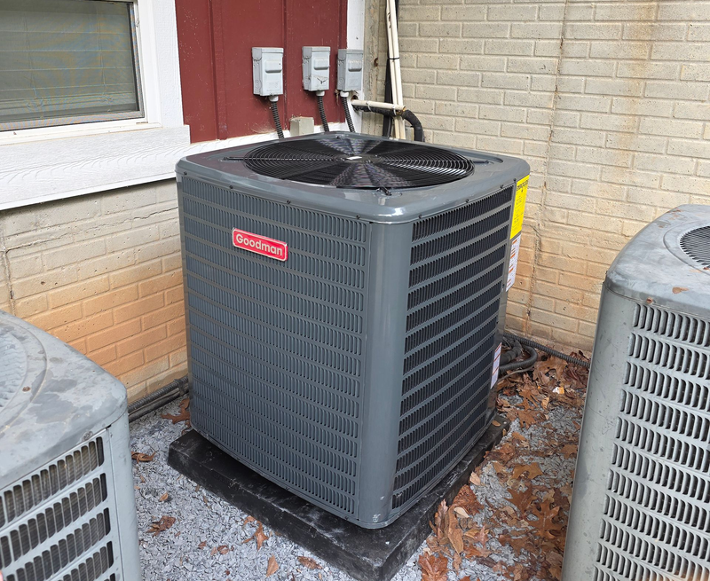 Outdoor air conditioner unit beside a house wall, with two similar units partially visible nearby.