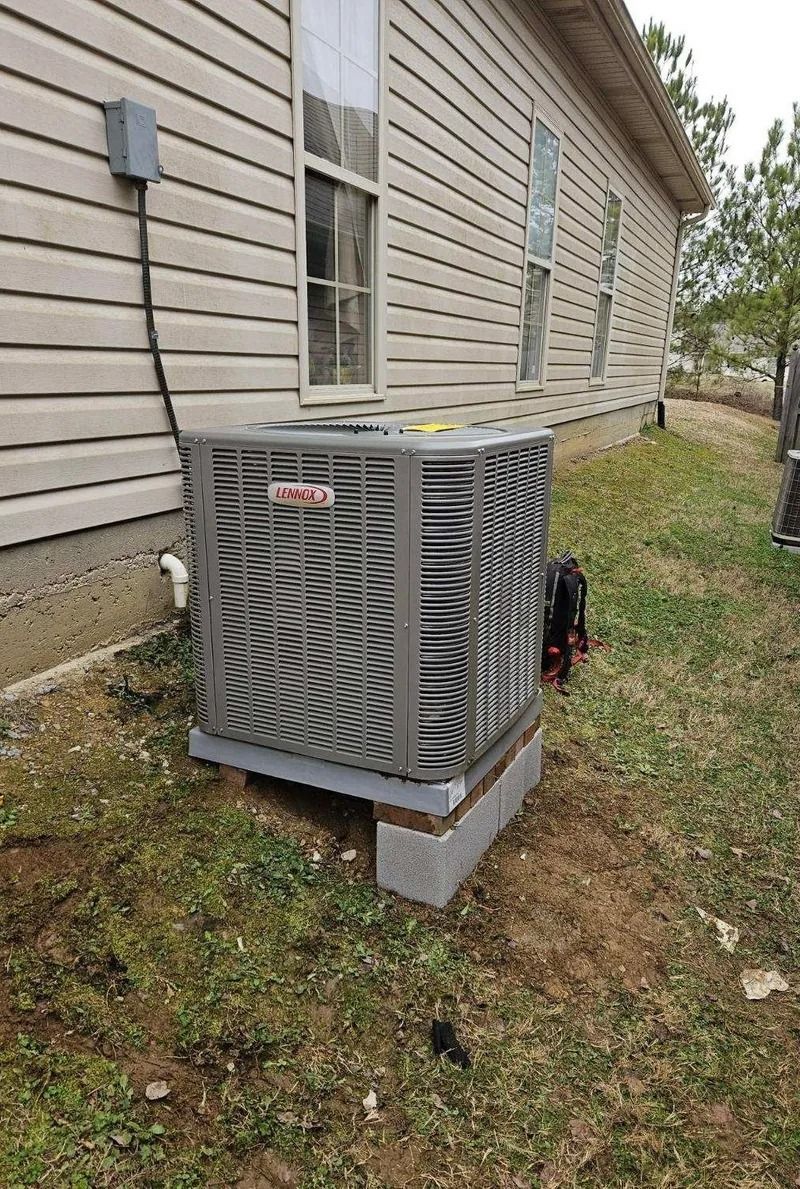 Outdoor air conditioner unit beside a beige house on a concrete pad in a grassy yard
