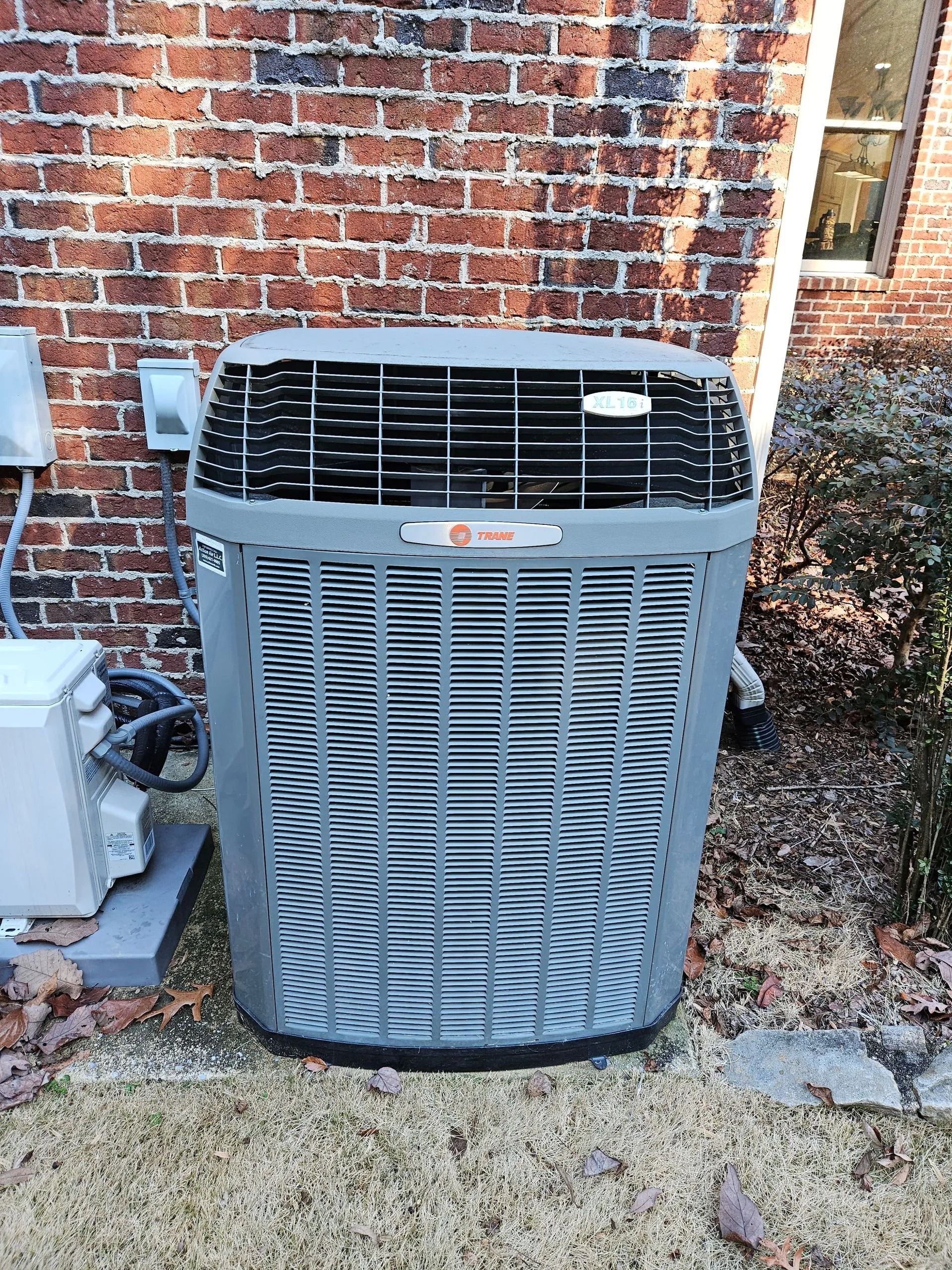Outdoor HVAC unit beside a brick wall, with a second unit partly visible on the left.