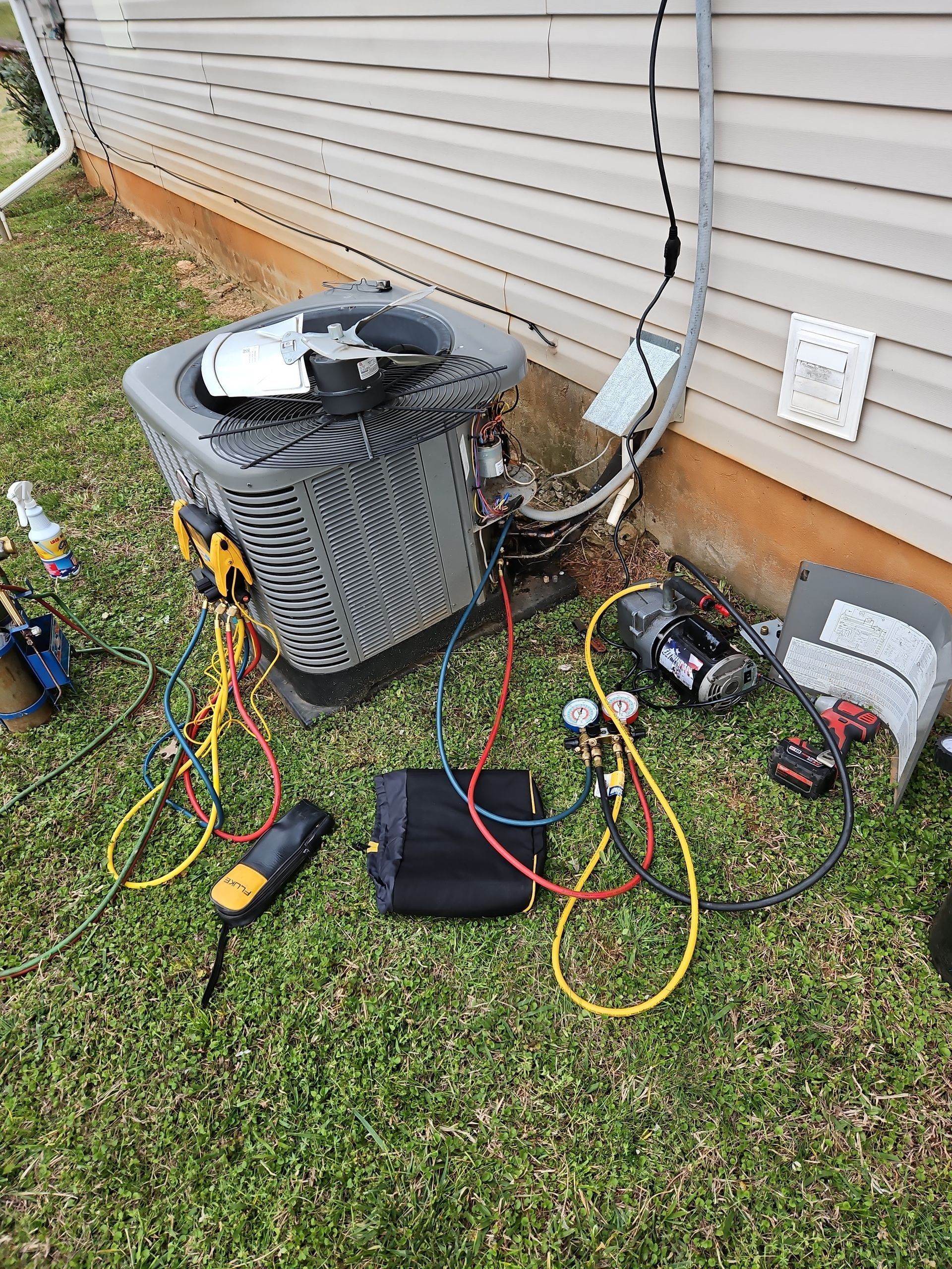 Air conditioner with scattered tools, cables, and repair equipment beside a house exterior.