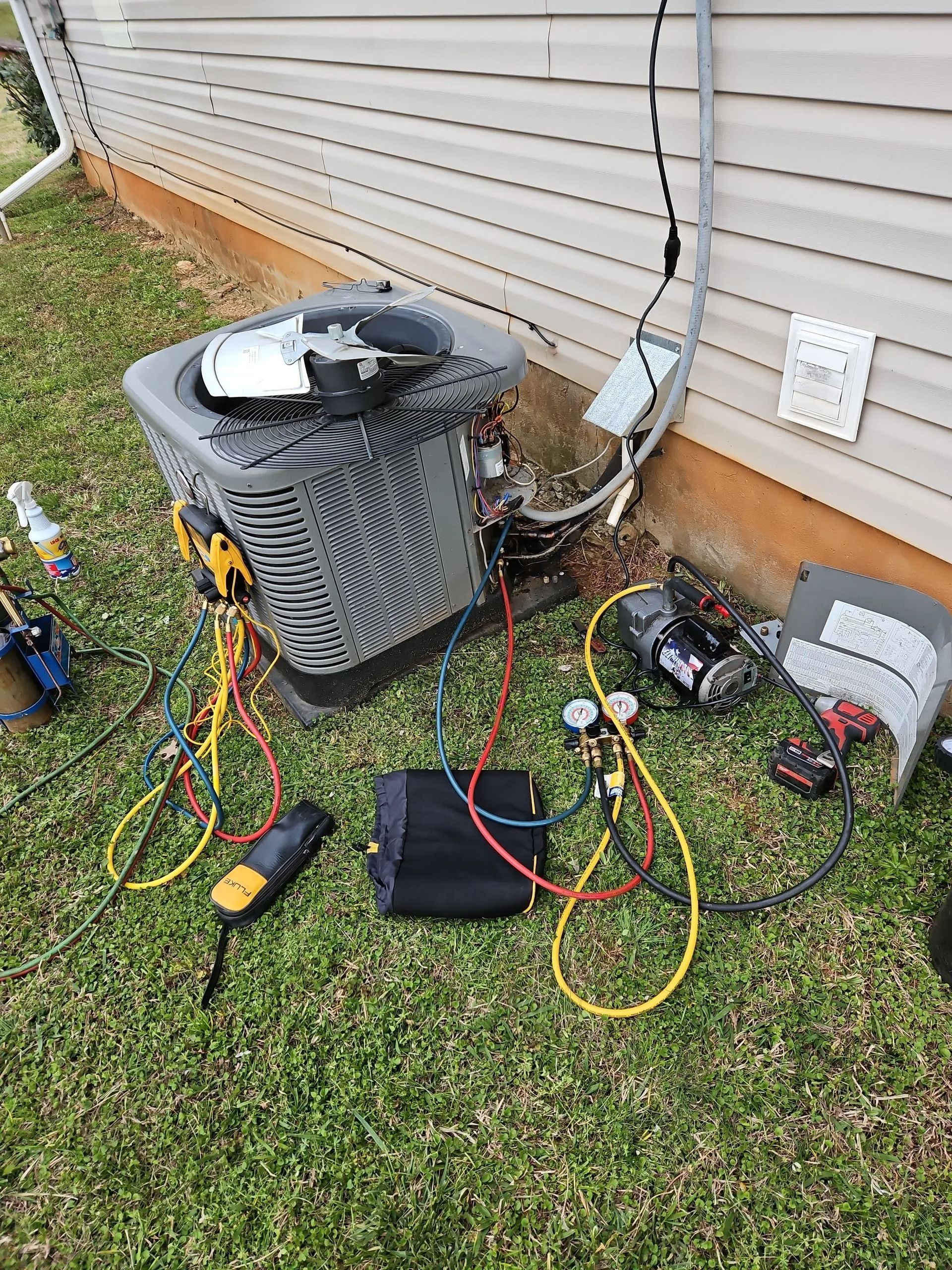 Outdoor HVAC unit with tangled electrical cords and tools beside a house wall