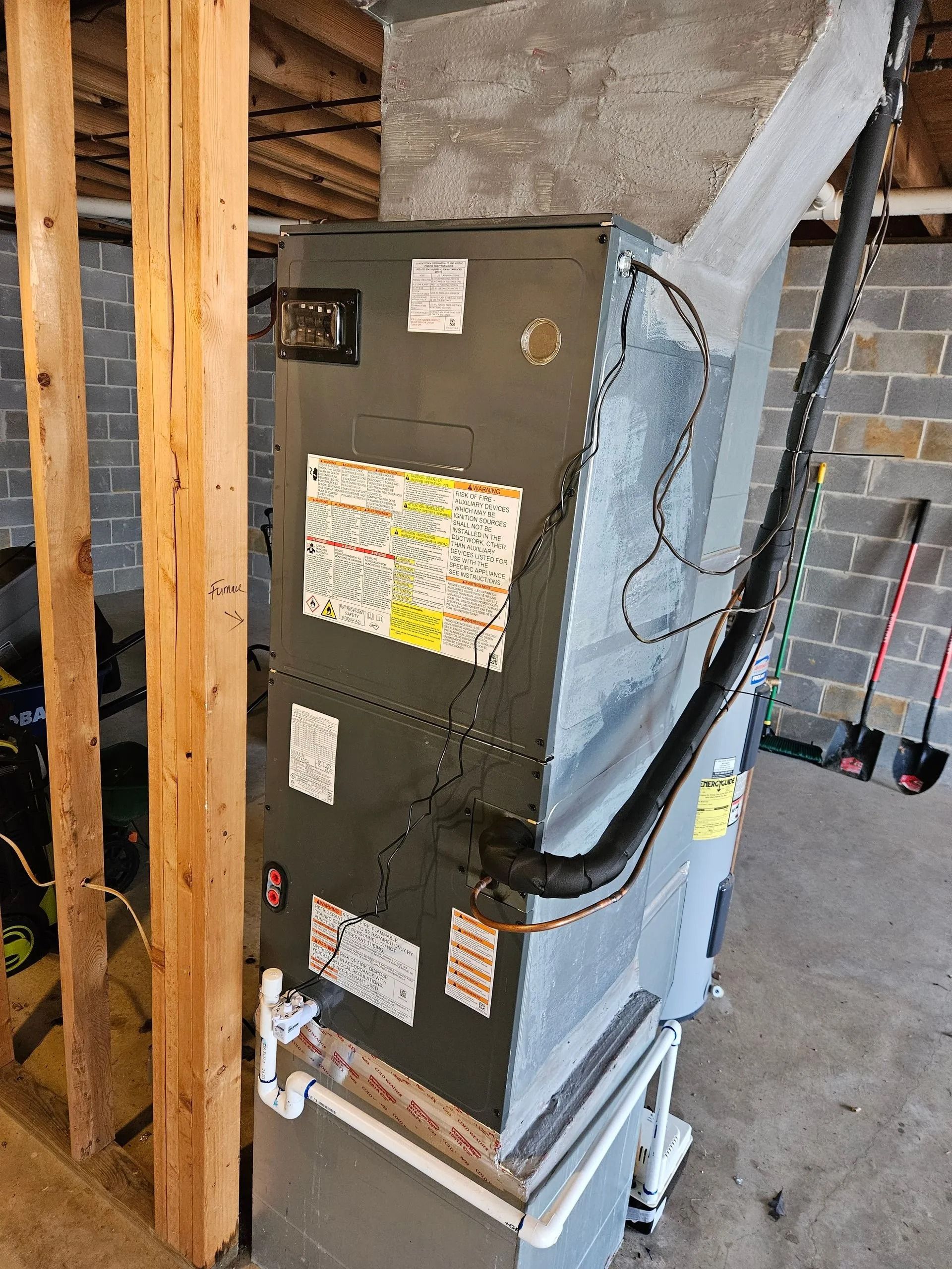Old HVAC furnace unit in a basement, wrapped with blue insulation and surrounded by unfinished framing.