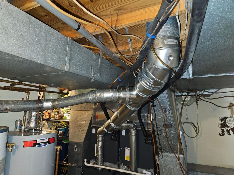 Basement mechanical room with insulated metal ducts, pipes, wires, and a water heater.