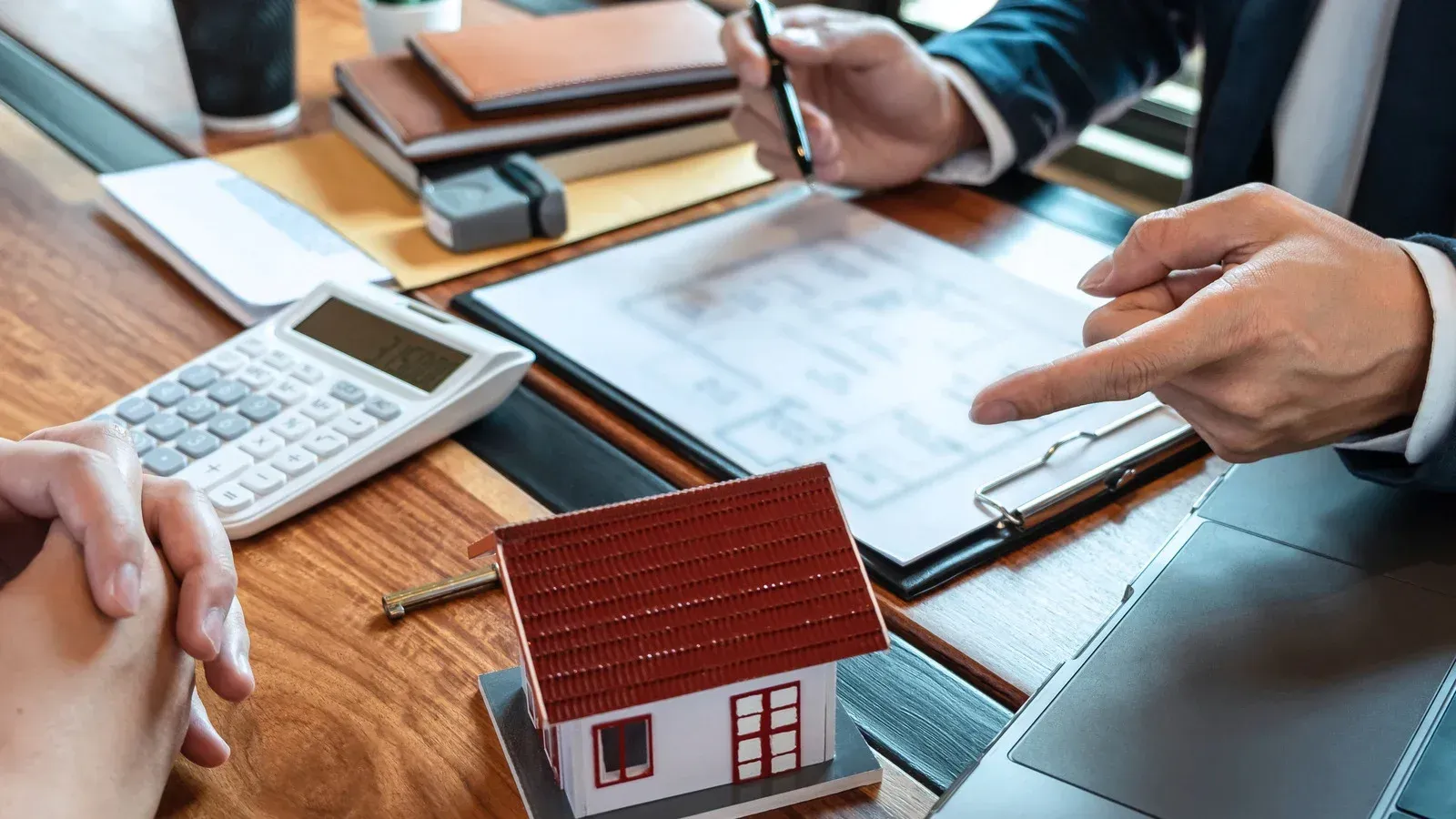 A man is sitting at a table with a model house and a calculator.