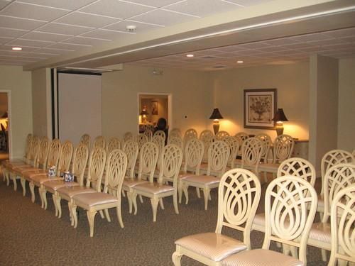 Rows of cream-colored chairs in a beige-walled room, likely a venue for gatherings or presentations.