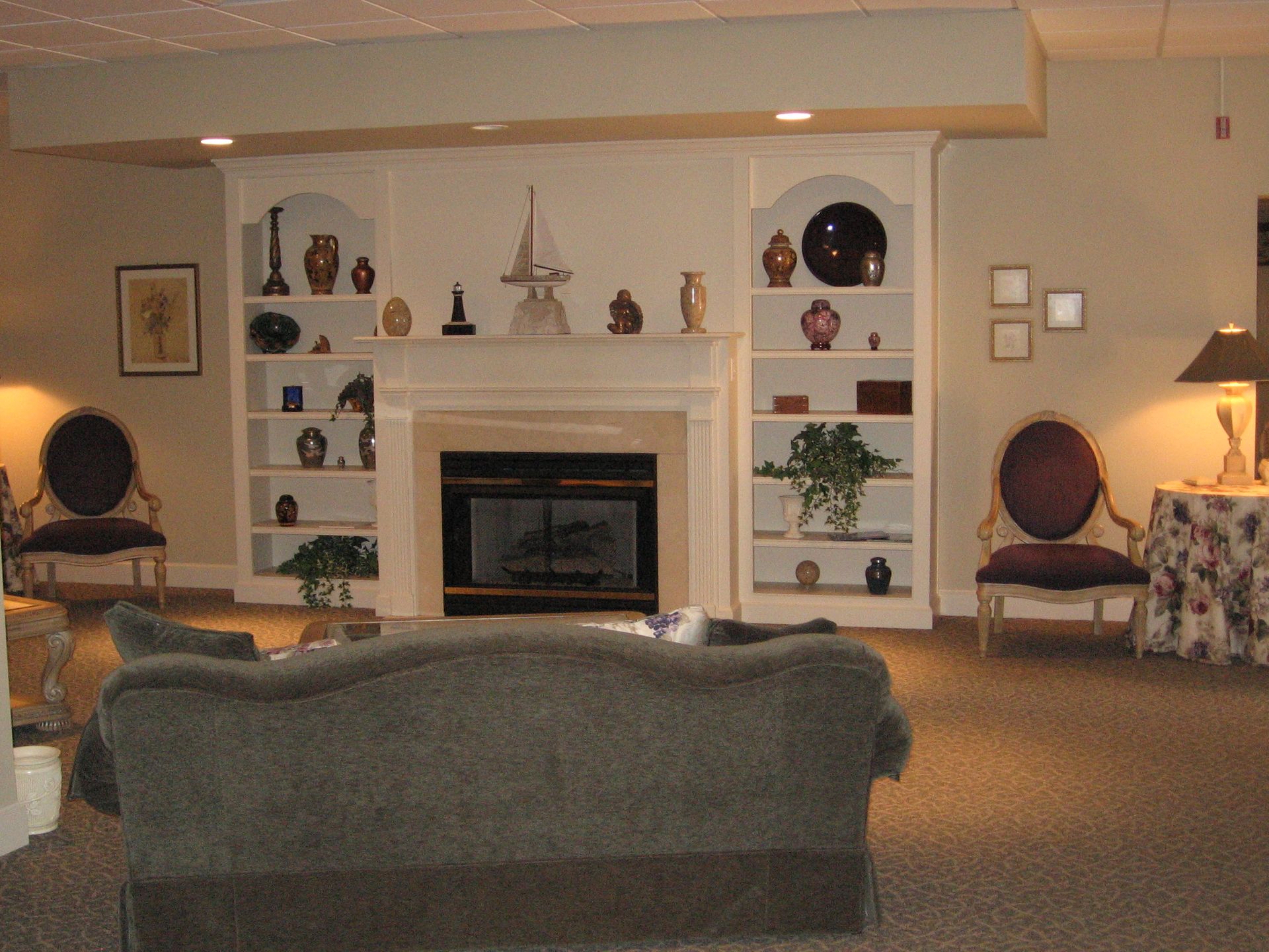 Cozy living room with fireplace, built-in shelves, sofa, and chairs. Warm lighting and decorative items.