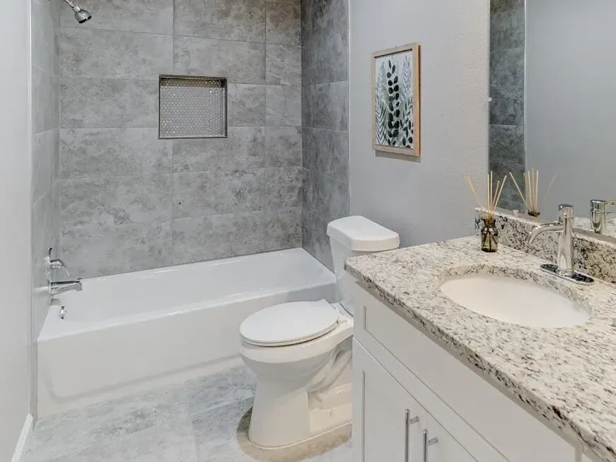 Modern bathroom with a white tub, toilet, marble vanity, and gray tiled walls