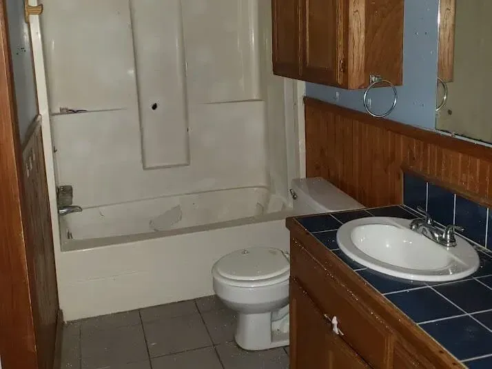 Small bathroom with bathtub, toilet, and sink, featuring wood cabinets and blue tile accents.