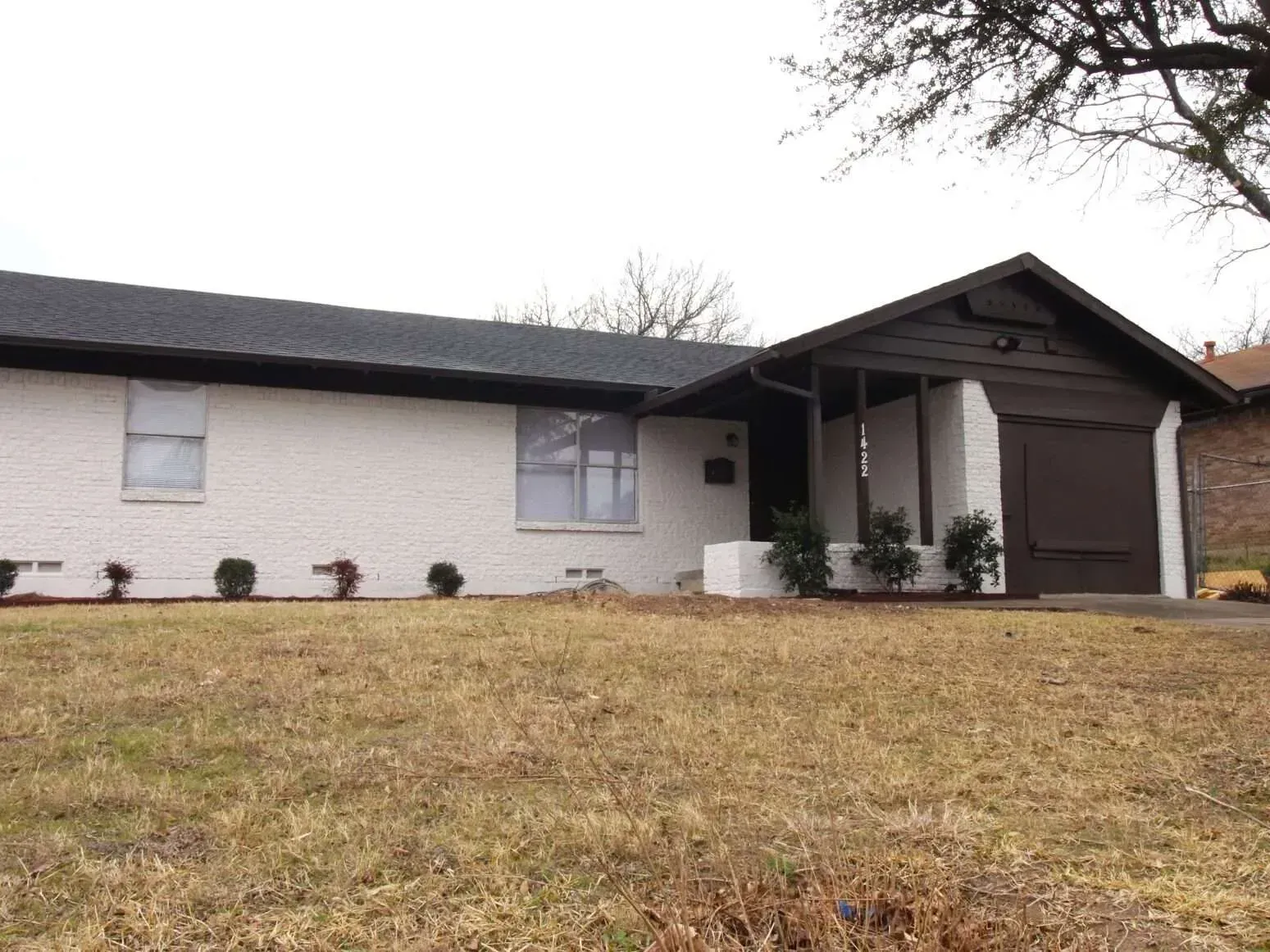 Single-story house with white brick, dark roof, and attached garage on a grassy slope.