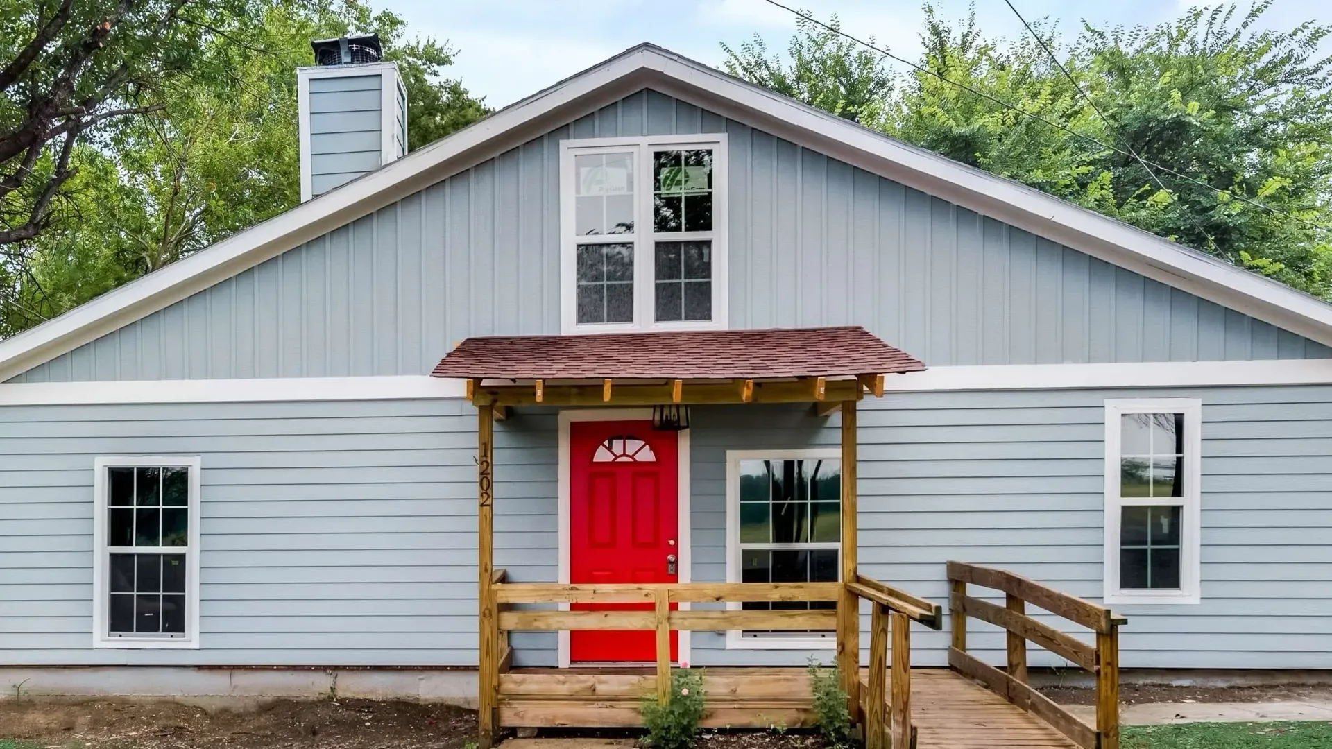 Small white house with red front door, porch, and ramp, set in a grassy yard.