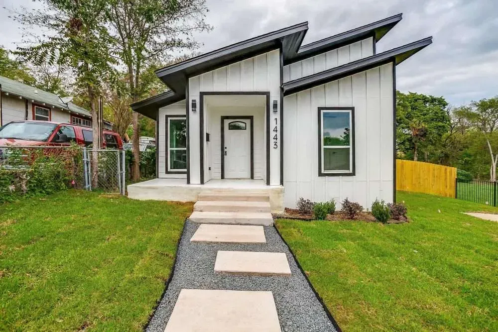 Small modern white house with a front walkway, lawn, and black roof accents