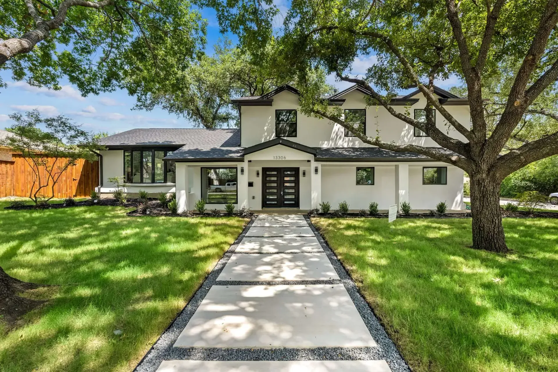 Modern two-story house with white exterior, large oak tree, and a stone walkway through a green lawn