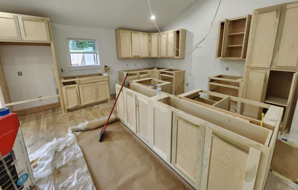 Unfinished kitchen with bare wood cabinets and counters under construction, floor covered with protective plastic.