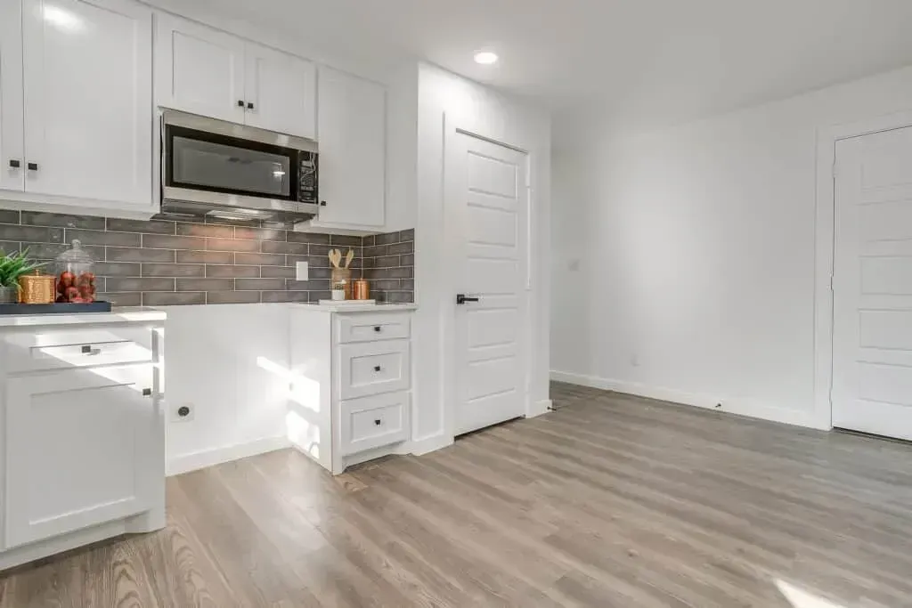 Bright white kitchen with stainless appliances, tile backsplash, and light wood flooring