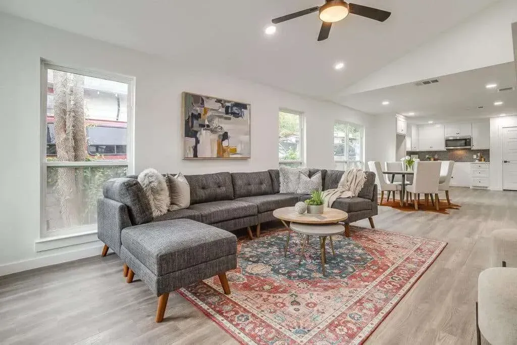 Bright modern living room with gray sectional, red patterned rug, coffee table, and kitchen view