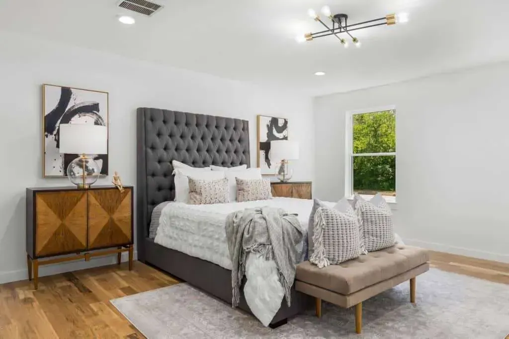 Modern bedroom with tufted gray bed, wooden nightstands, bench, and abstract wall art