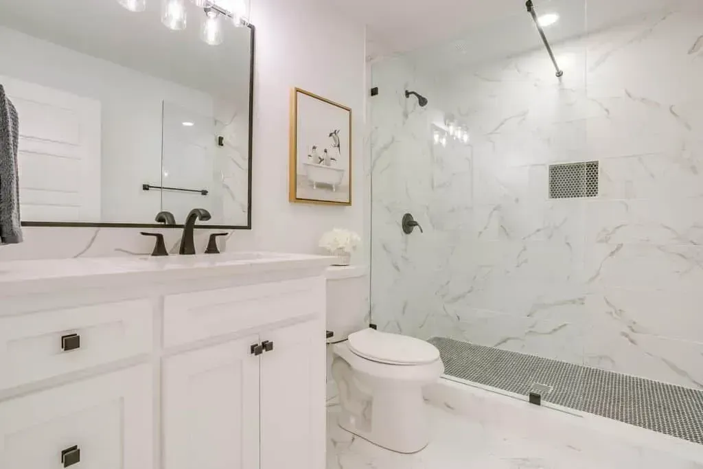 Bright white bathroom with vanity, mirror, and glass-enclosed shower with marble tile.