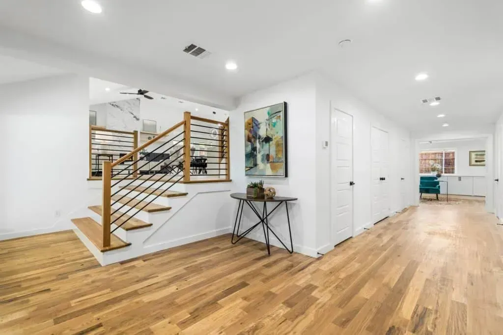 Bright modern hallway with wood floors, floating staircase, wall art, and a small console table