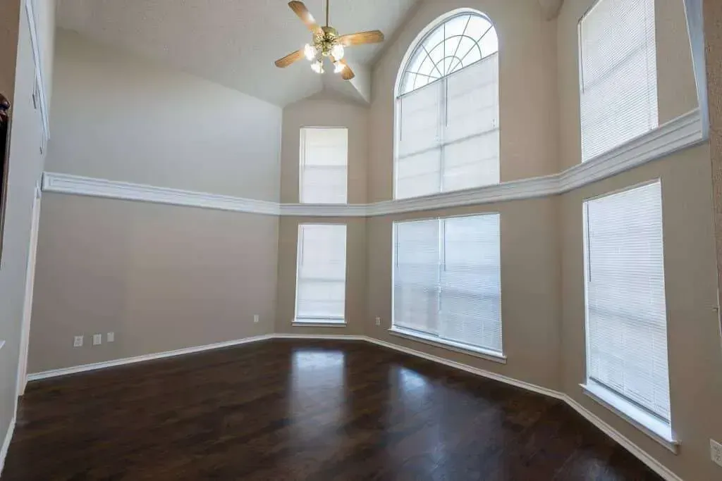 Empty bright living room with tall arched windows, dark hardwood floors, and a ceiling fan