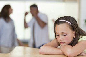 girl leaning on table with parents arguing behind her
