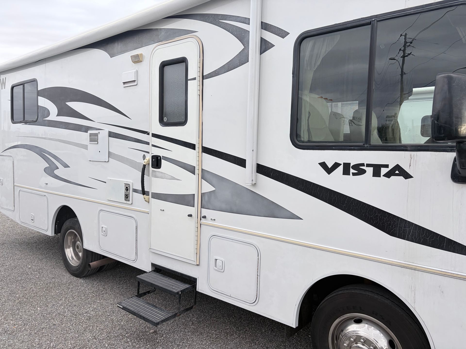 White RV with "Vista" on the side, parked outdoors on a gray surface. It has a door, windows, and awning.