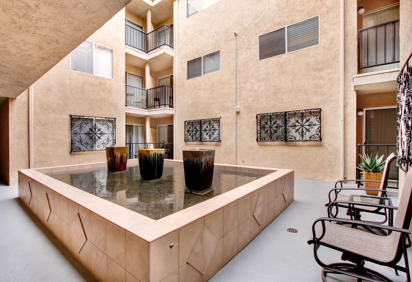Courtyard with a central fountain, beige apartment walls, and wrought-iron chairs