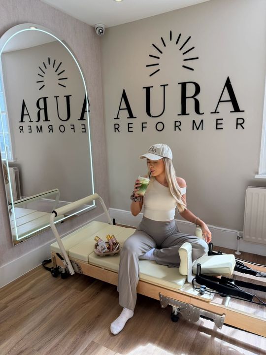 Woman in workout clothes using a pilates machine, kneeled position, arm extended with strap.