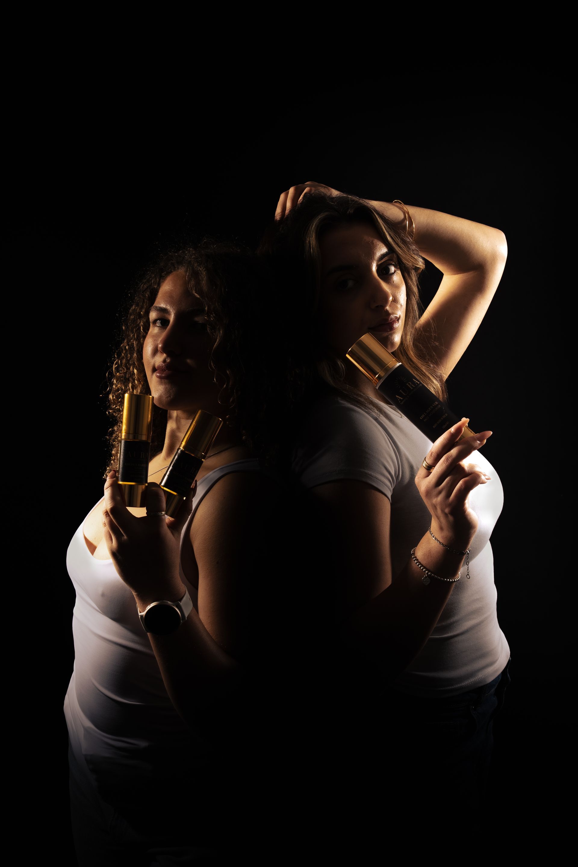 Two women posing back-to-back in low light, each holding a paintbrush against a black background.