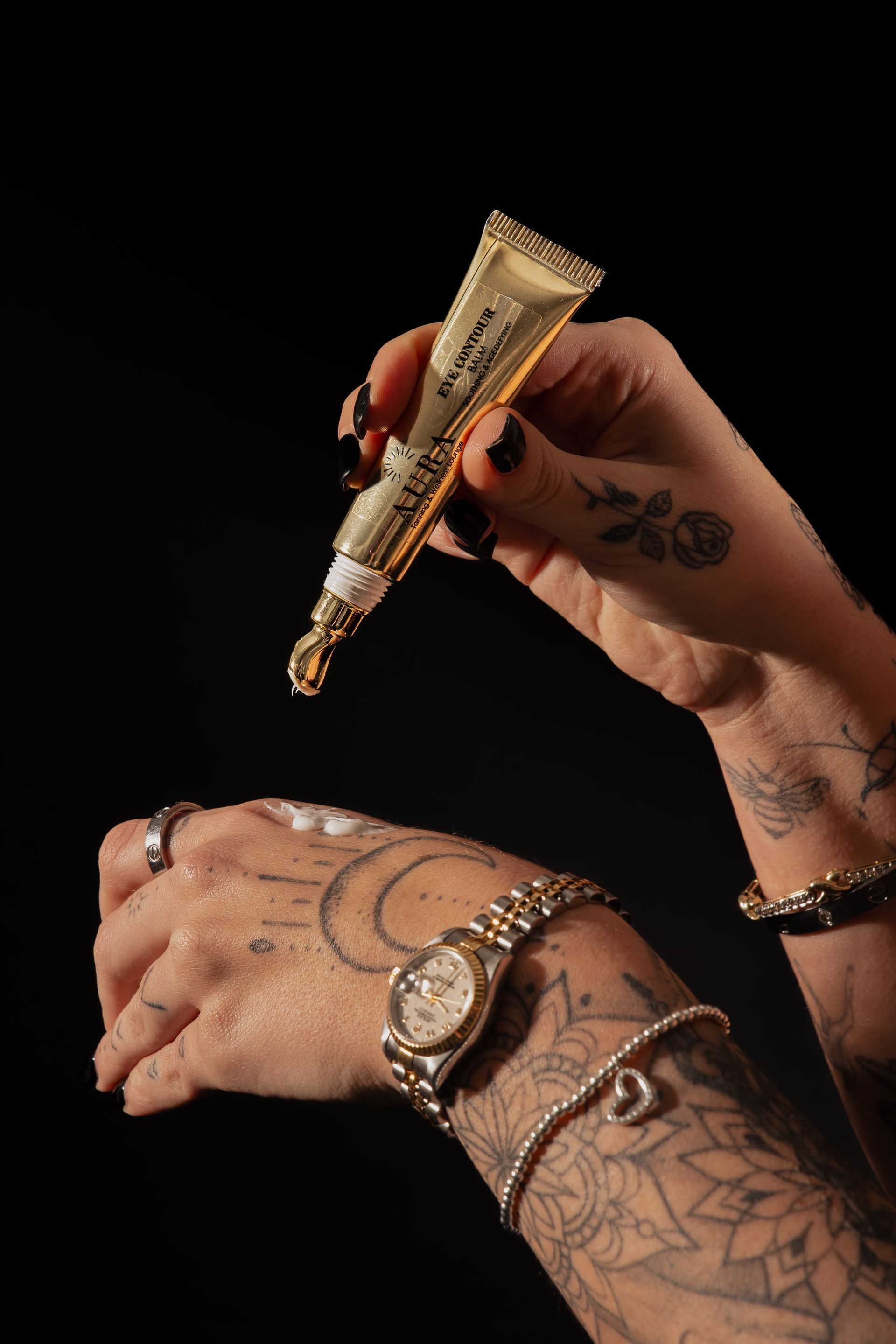 Hand holding a gold tattooing pen over a tattooed forearm against a black background