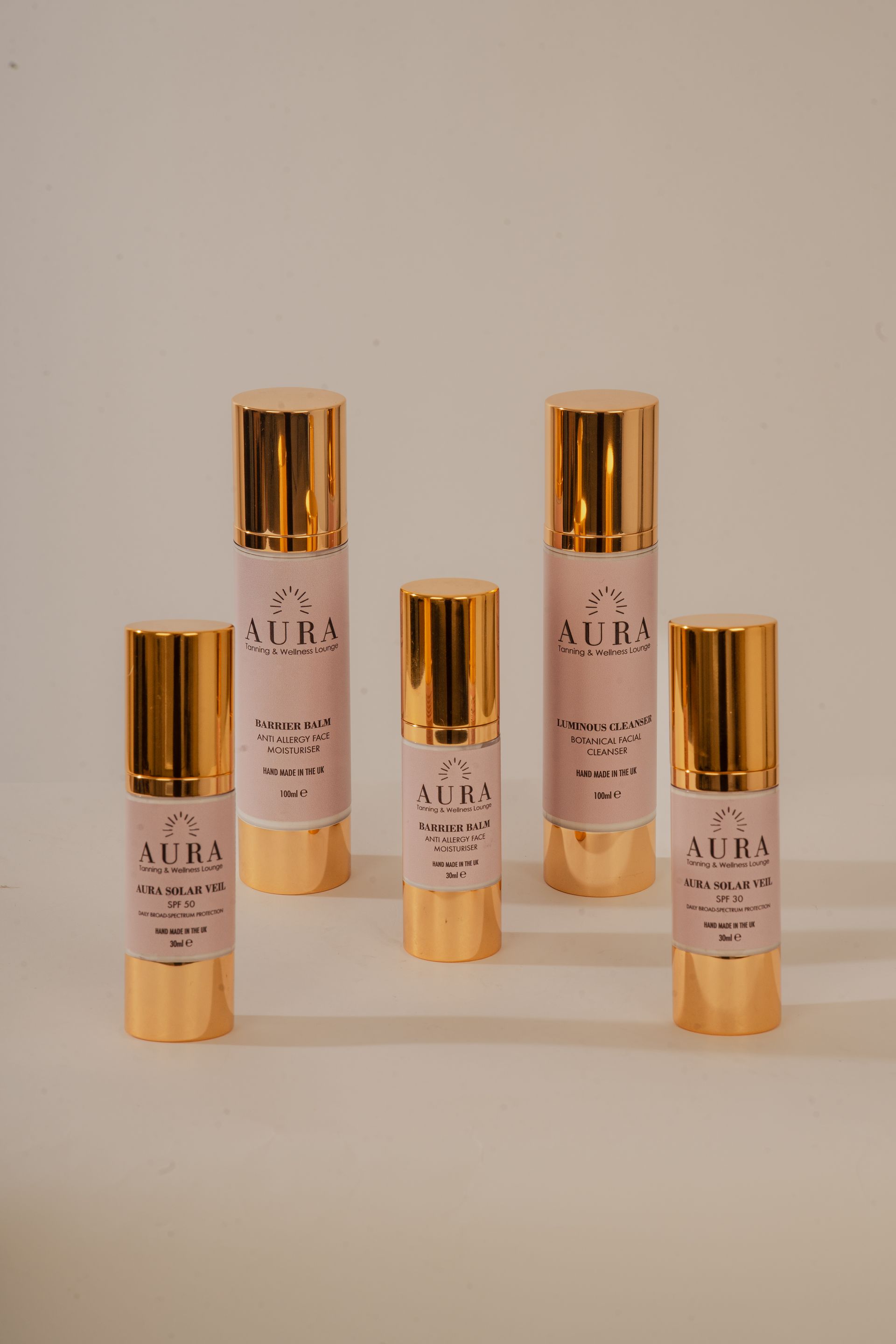 Five gold-capped cosmetic serum bottles on a beige background