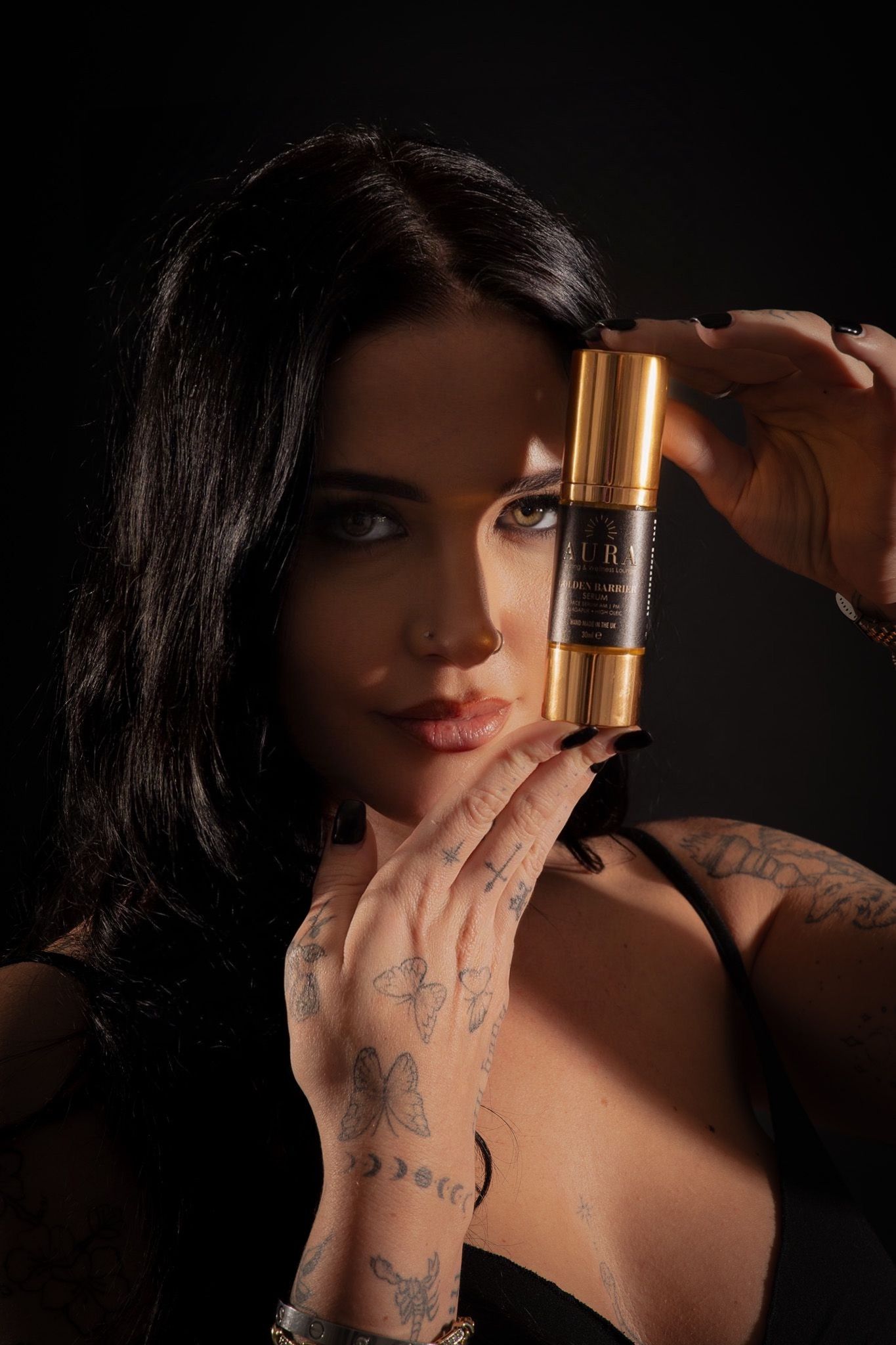 Woman holding a gold lipstick tube near her face in dramatic low light