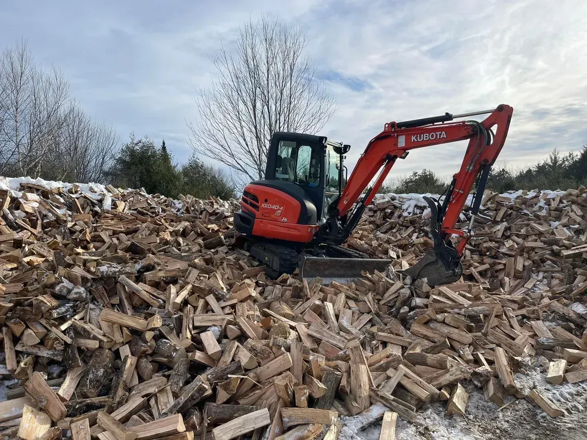 Red excavator digging through a large pile of wood debris in a snowy outdoor area