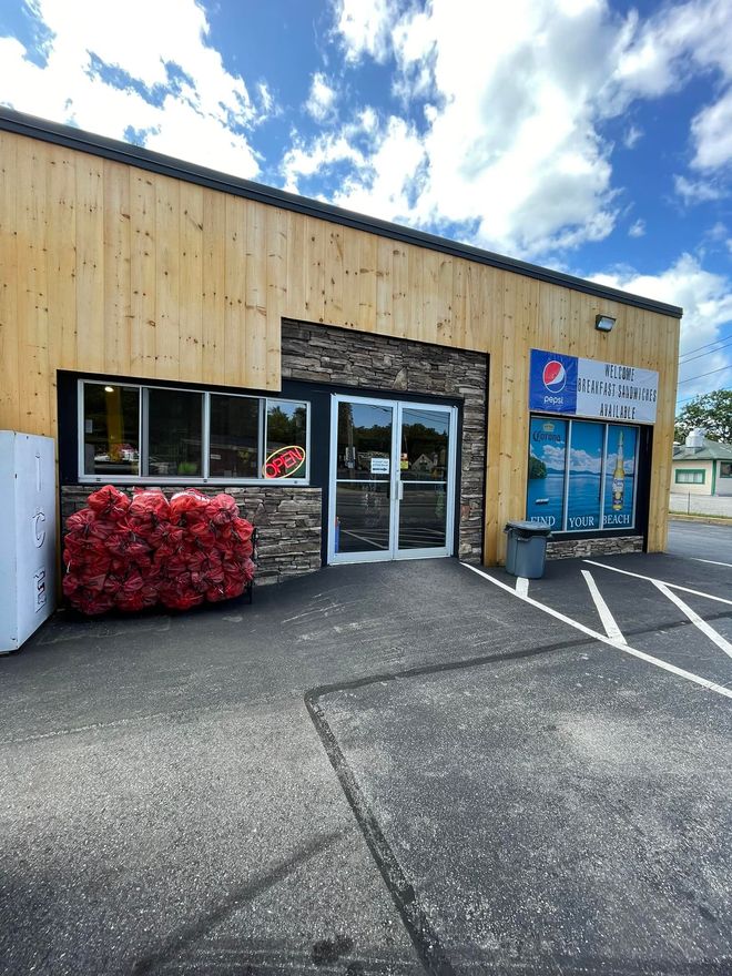 Small storefront with blue door, Pepsi sign, and red shrub in front of a wooden building