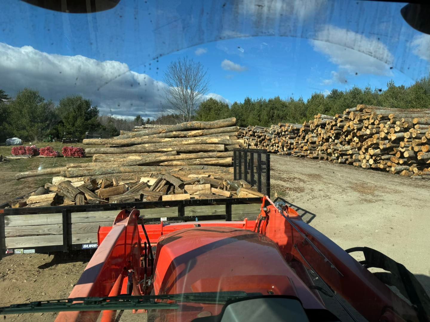 View from a red tractor at a lumber yard with stacked logs and blue sky