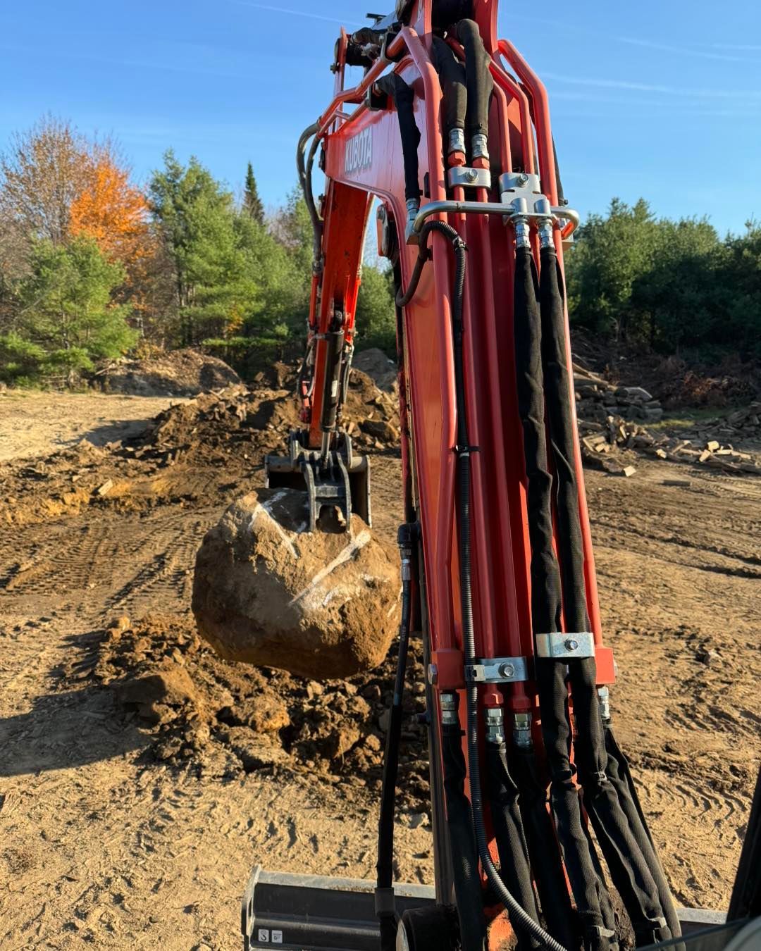Red excavator arm with bucket digging in a dirt clearing under a blue sky
