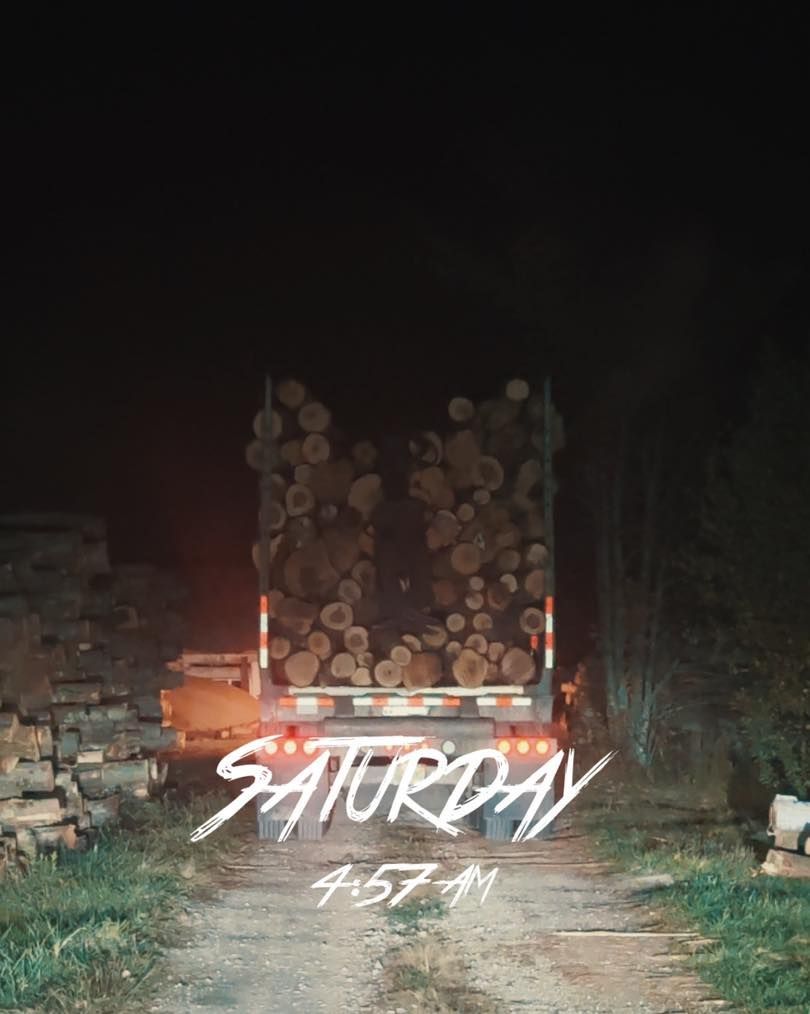 Stacked logs on a truck at night with “Saturday” written in white text over the scene.