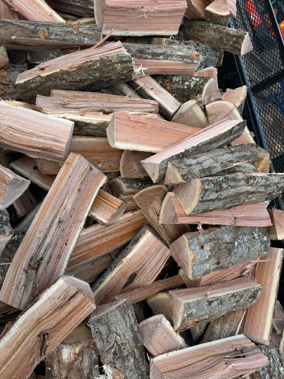 Stacked split firewood logs in a pile, showing rough bark and cut wood ends