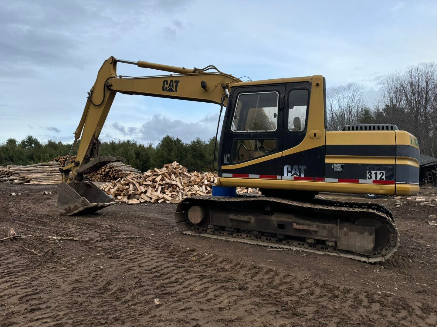 Yellow CAT excavator digging a dirt pile at a construction site under a cloudy sky