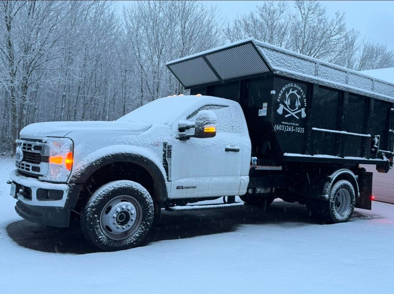 Snow-covered white and black dump truck parked in a snowy lot with frosty trees in the background