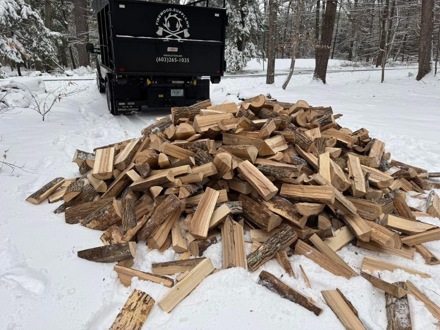 Pile of split firewood in snow behind a black truck in a winter forest