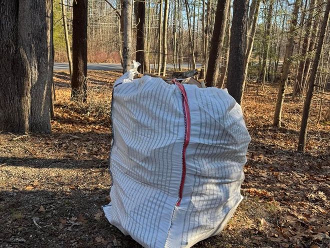 White wrapped bale in a wooded area with fallen leaves and bare trees