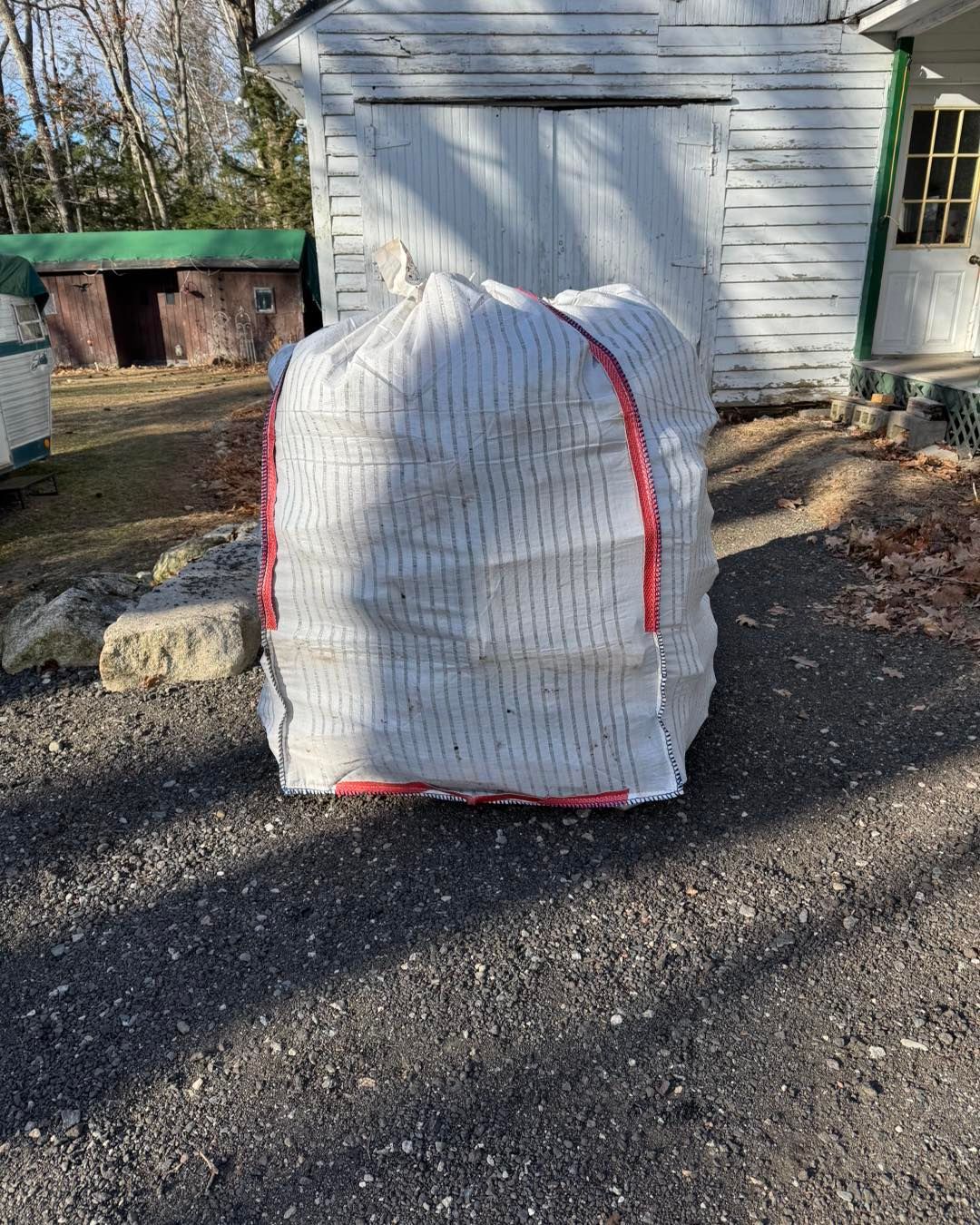White bagged object with red straps sitting on gravel in front of a white garage