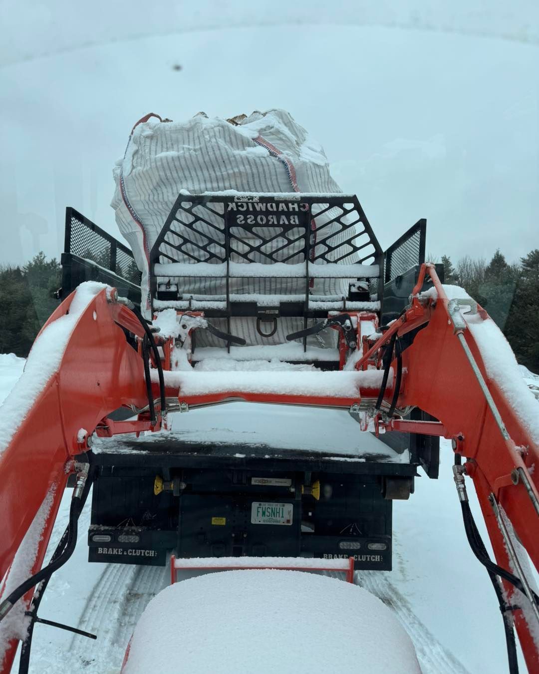 Snow-covered orange tractor facing a snow-packed truck and gate in a winter yard