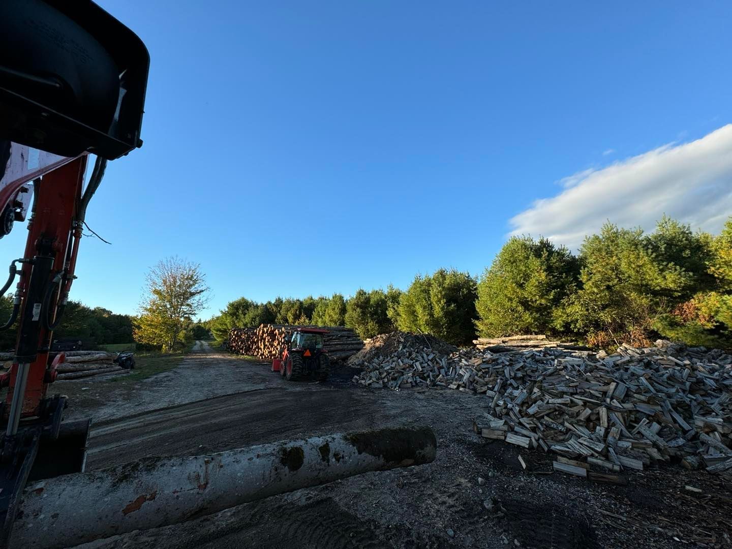 Construction site with gravel piles, a large pipe, and trees under a clear blue sky