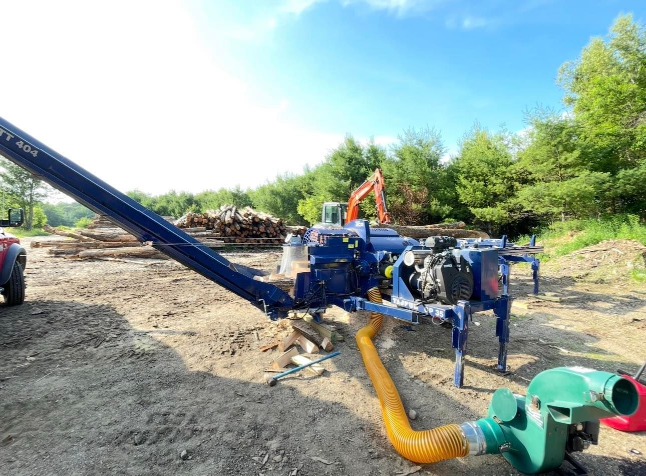 Blue industrial pump and orange excavator on a dirt site with hoses and trees in the background