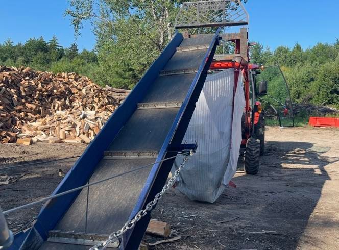 Blue conveyor belt loading wood chips into a truck in an outdoor yard