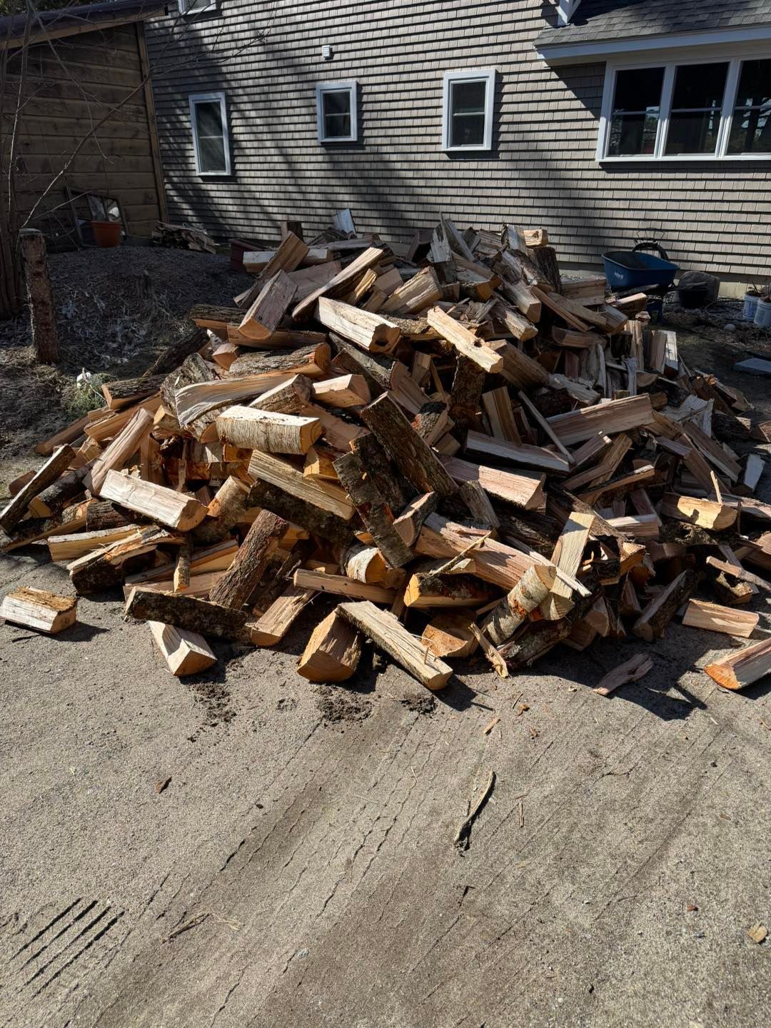 Pile of chopped firewood stacked on a driveway beside a house exterior