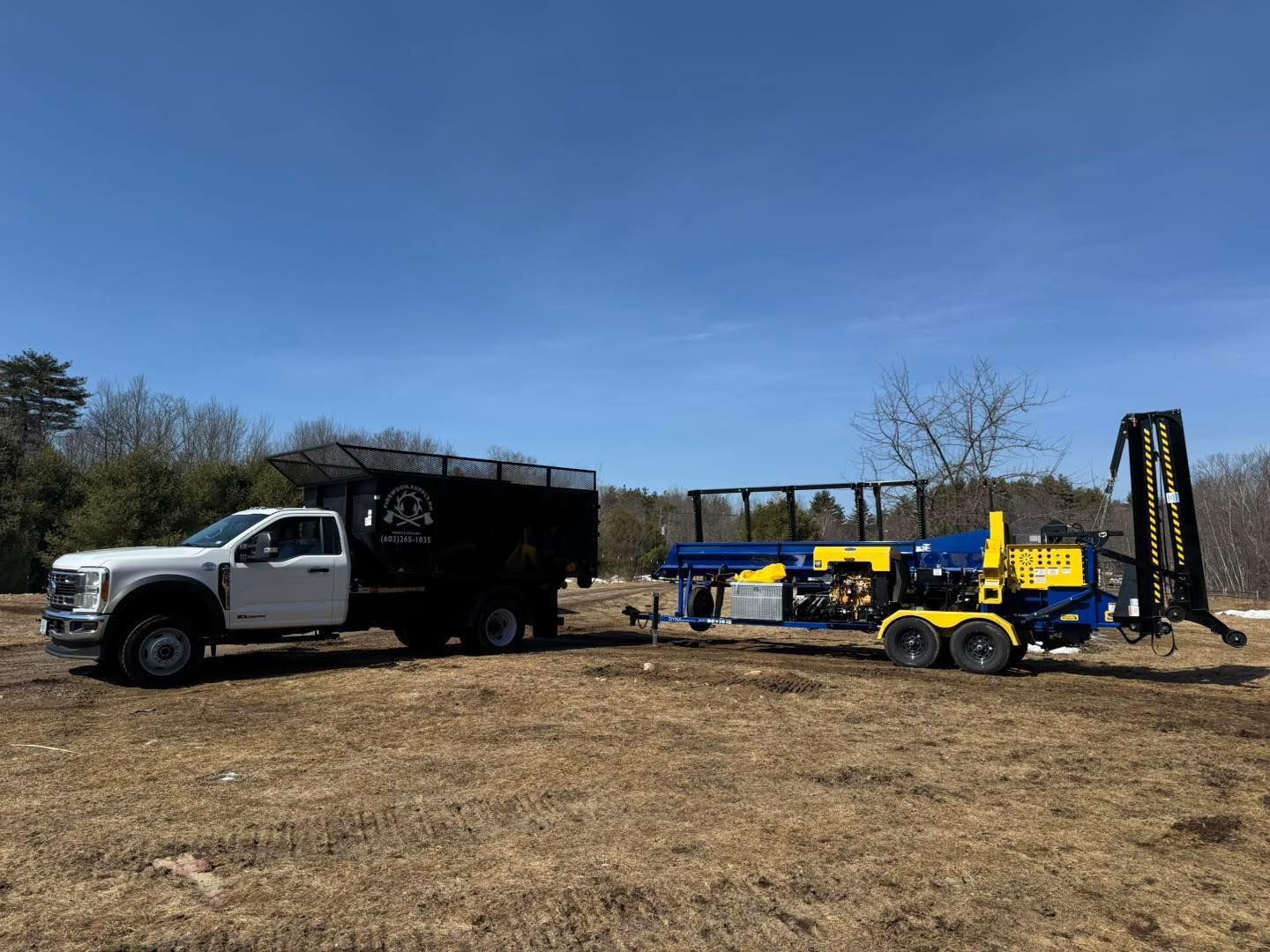 White truck and black box trailer beside a yellow drilling rig in a dry field under a blue sky