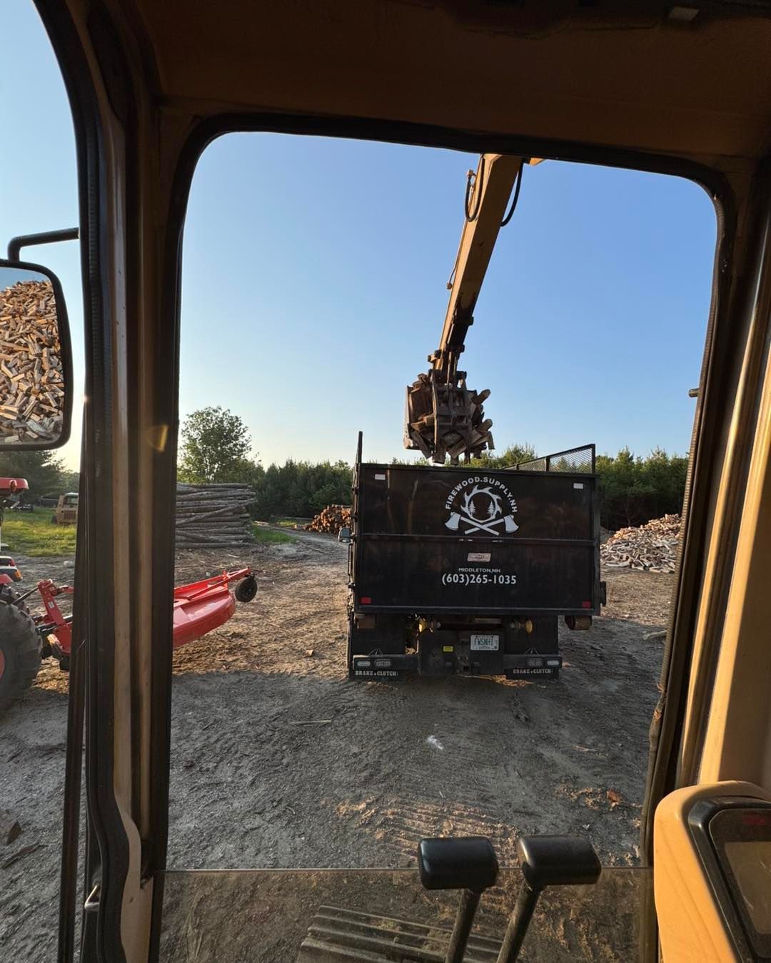 Excavator seen from a cab window, loading a truck at a dirt construction site under a clear blue sky.
