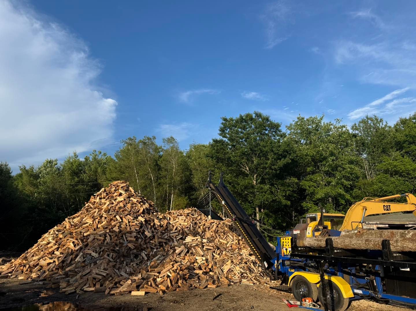 Yellow excavator beside a large wood chip pile under a blue sky